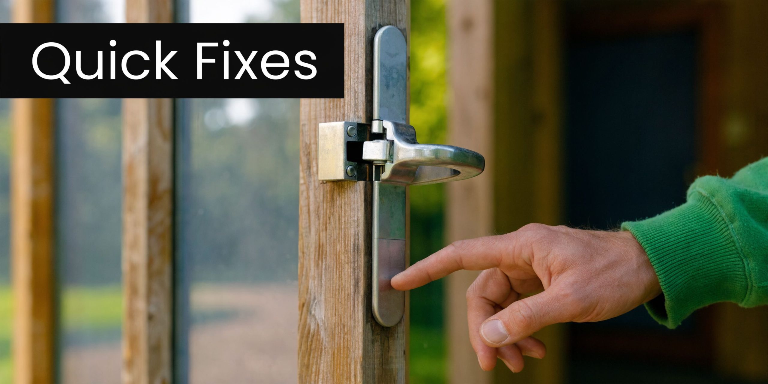 A hand touches the metal mechanism of a self locking gate latch on a wooden door frame.